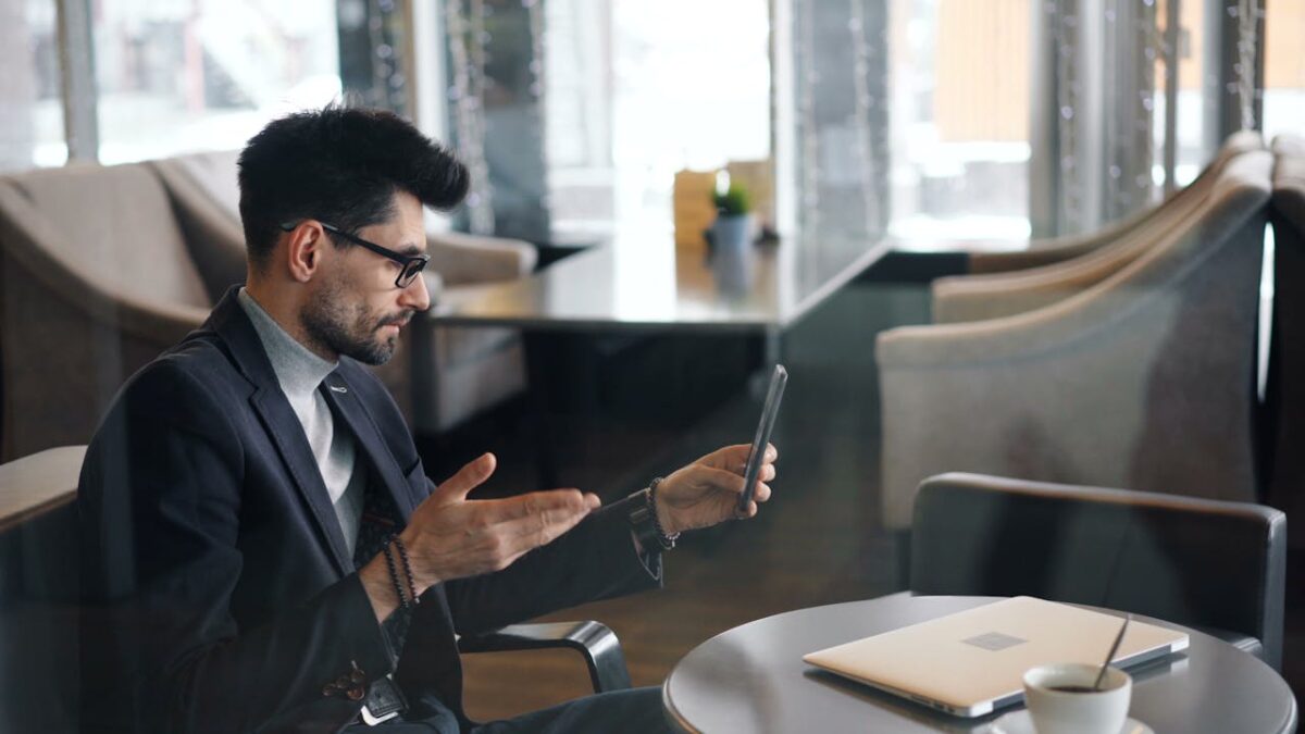 Businessman in a café using a smartphone for a video call, illustrating modern communication.