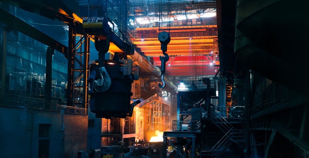 Inside a bustling steel factory with cranes and molten metal casting an intense glow.